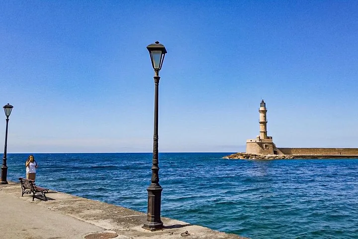 Femme marchant sur une jetée près d’un lampadaire, avec un phare au loin